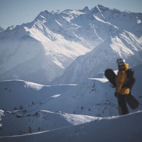 Snowboarder stands in front of an impressive mountain landscape