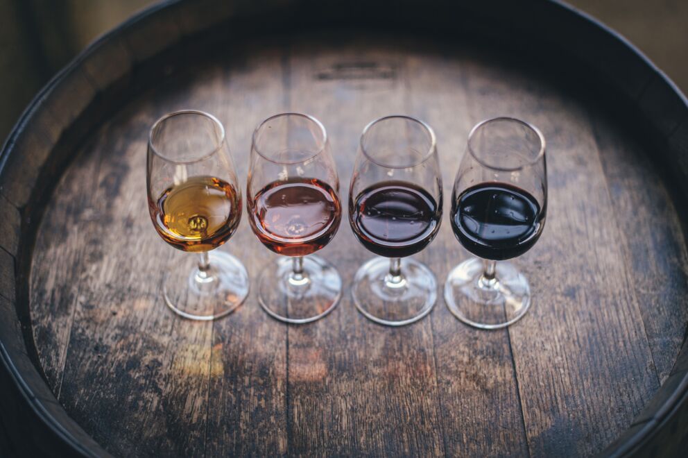 Vier Weingläser gefüllt mit unterschiedlichen Weinen auf einem Eichenfass