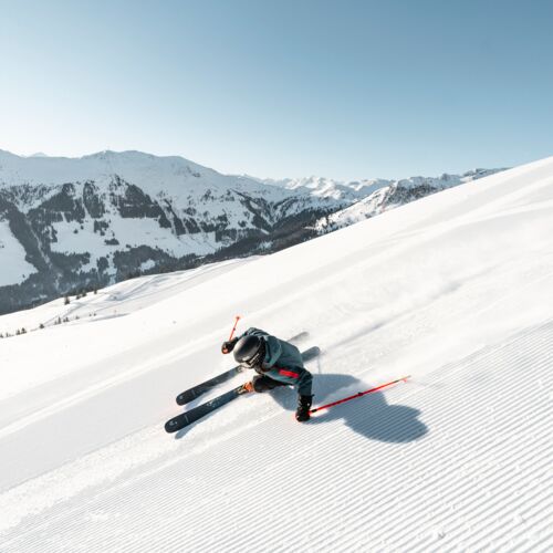 Skifahrer fährt über frisch präparierte Pisten mit Bergen im Hintergrund