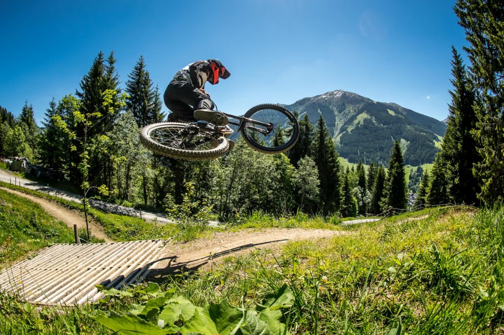 Downhill mountain biker jumps over a jump in an alpine setting
