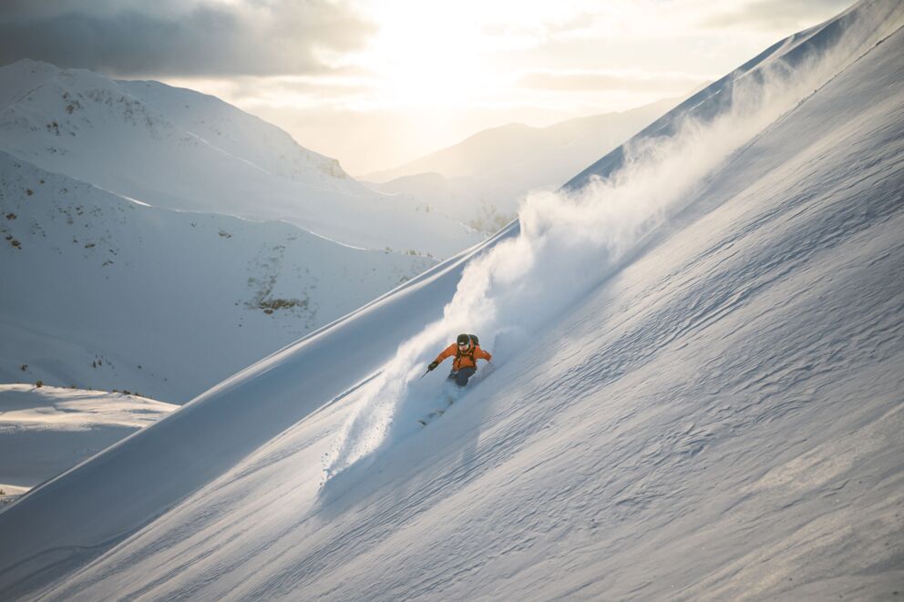 Skifahrer in orangenen Klamotten im Tiefschnee in den Alpen