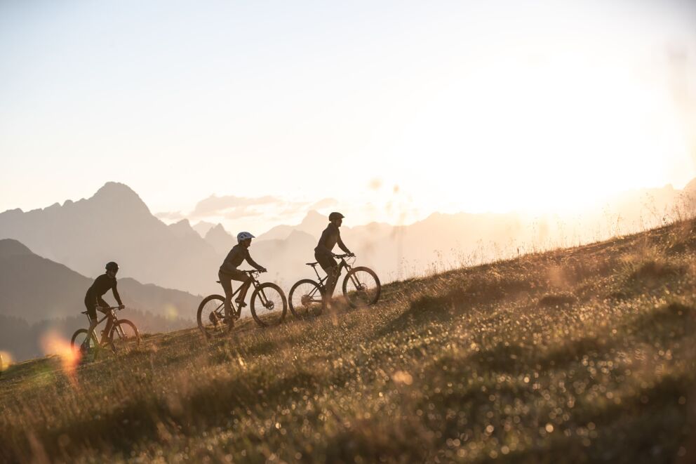 Three mountain bikers at sunrise shortly before the summit