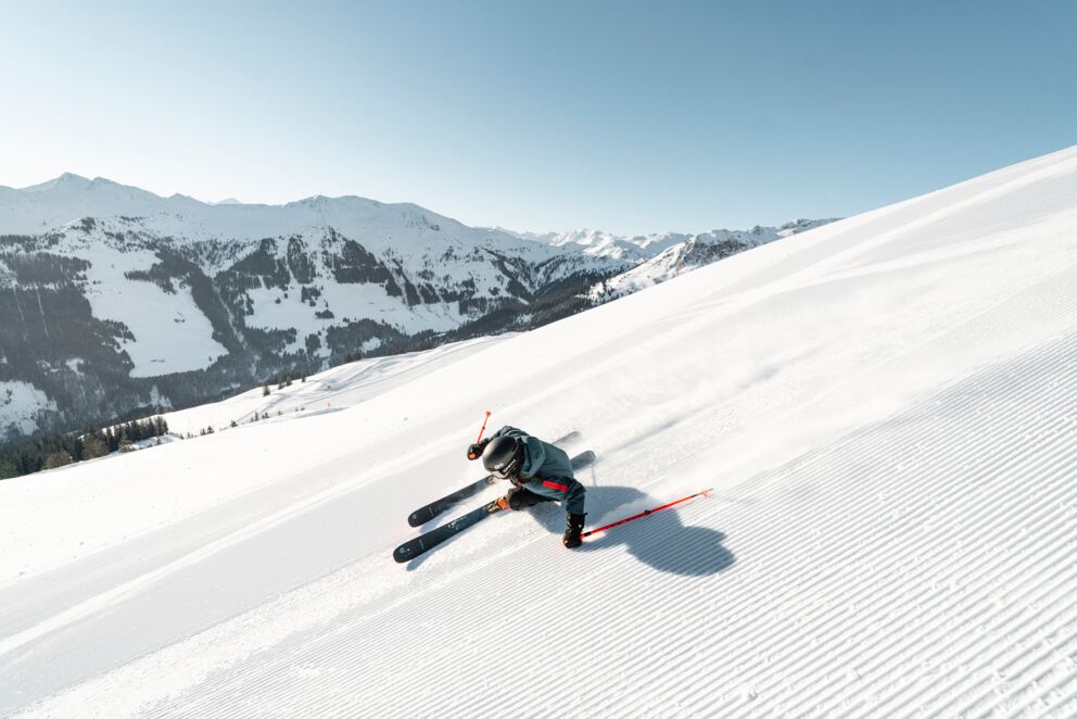 Skifahrer fährt über frisch präparierte Pisten mit Bergen im Hintergrund