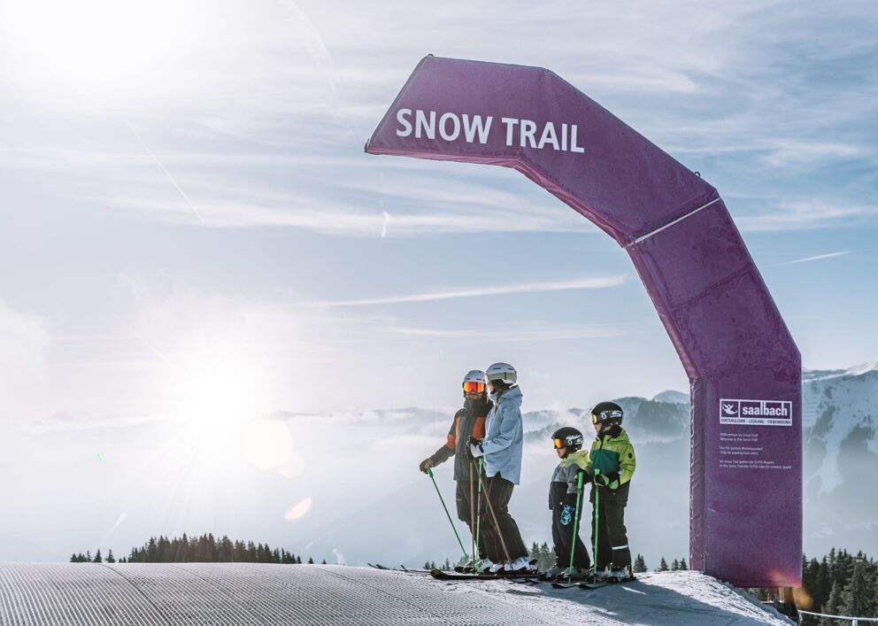 Familie mit zwei Kindern steht auf der Skipiste unter einem Bogen mit der Aufschrift "Snow Trail"