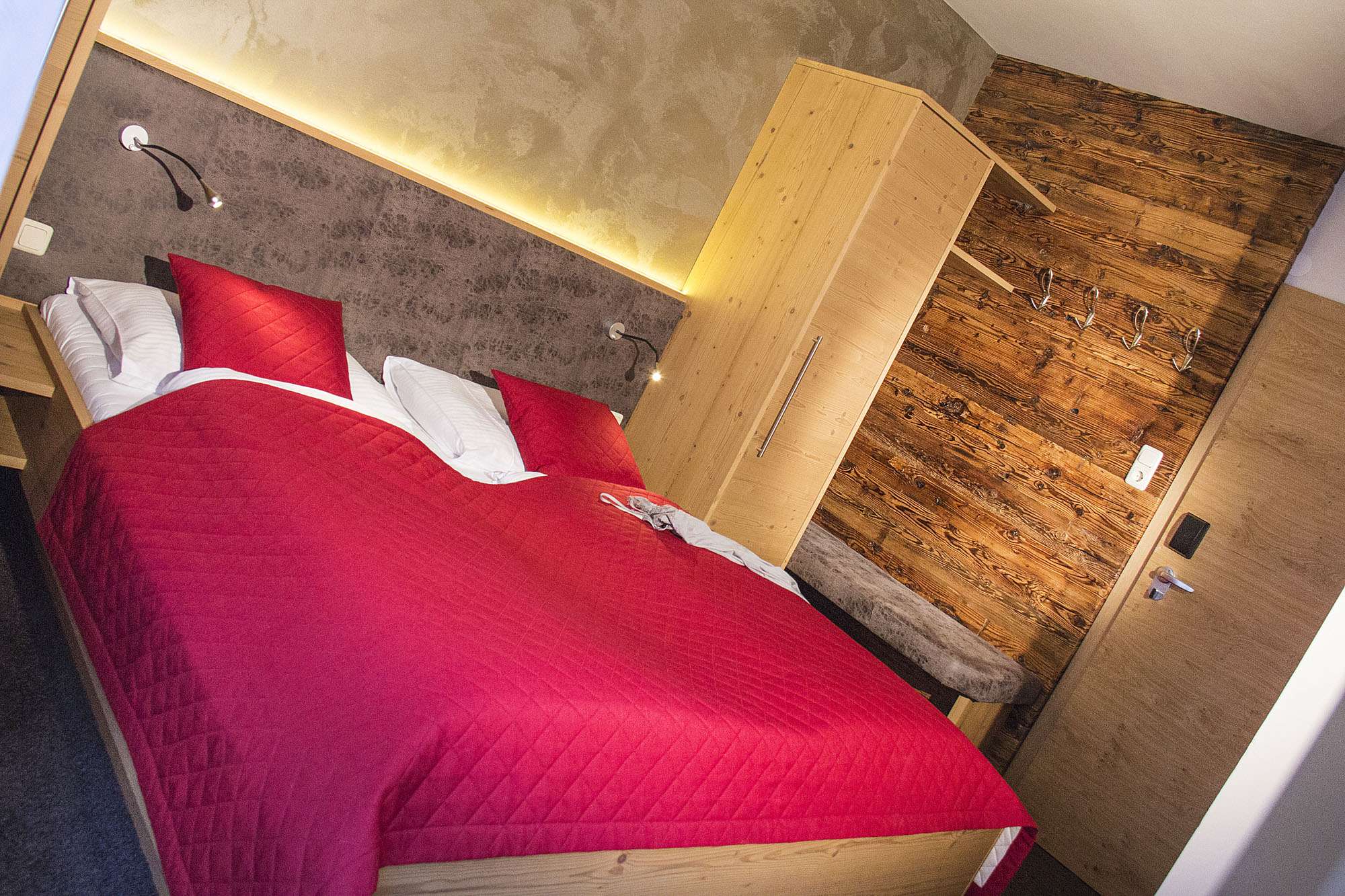 Hotel room with red wooden double bed in Hinterglemm