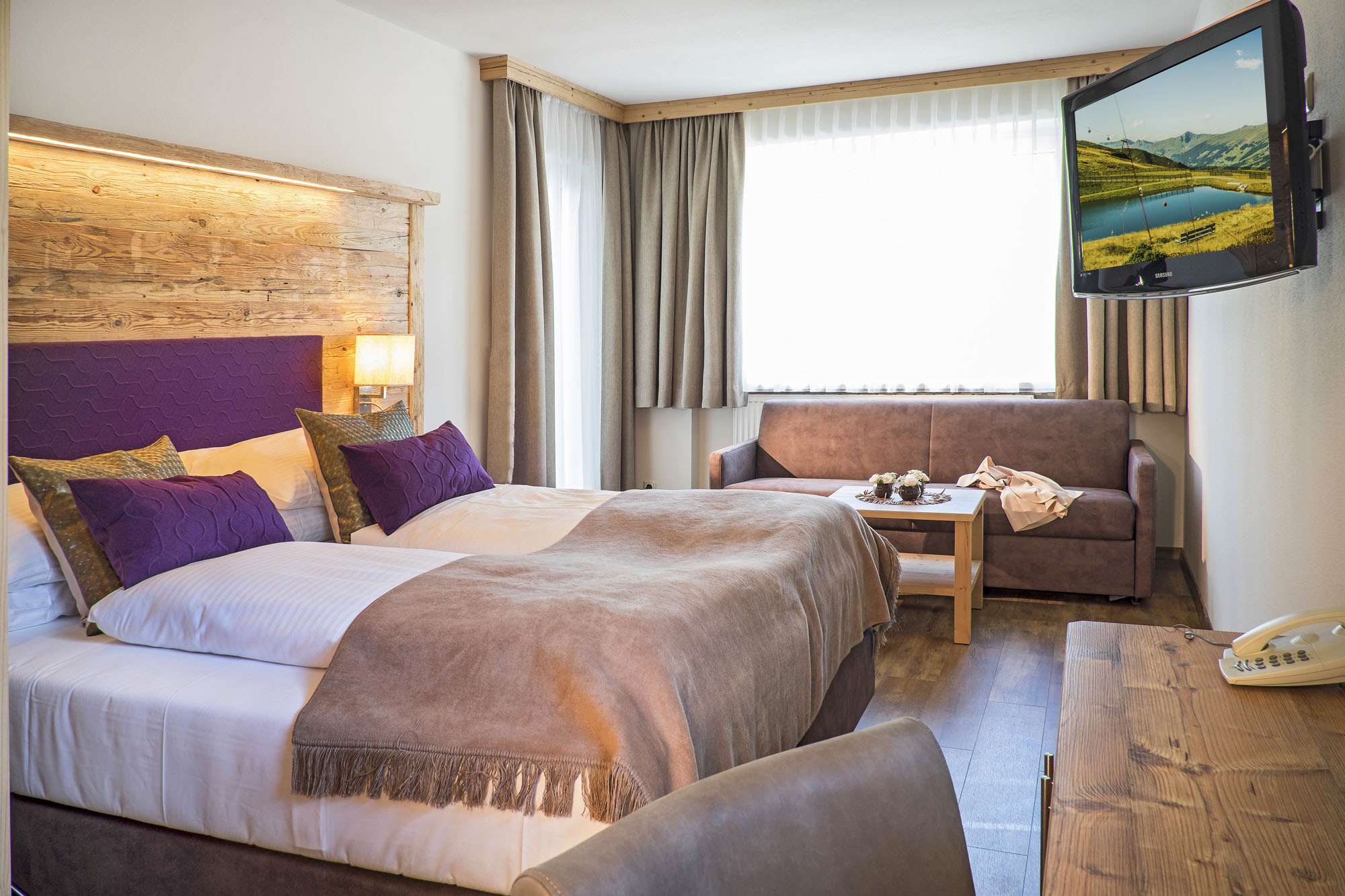 Modernes und helles Hotelzimmer in Hinterglemm mit einem Fernseher, Doppelbett und einem Sofa