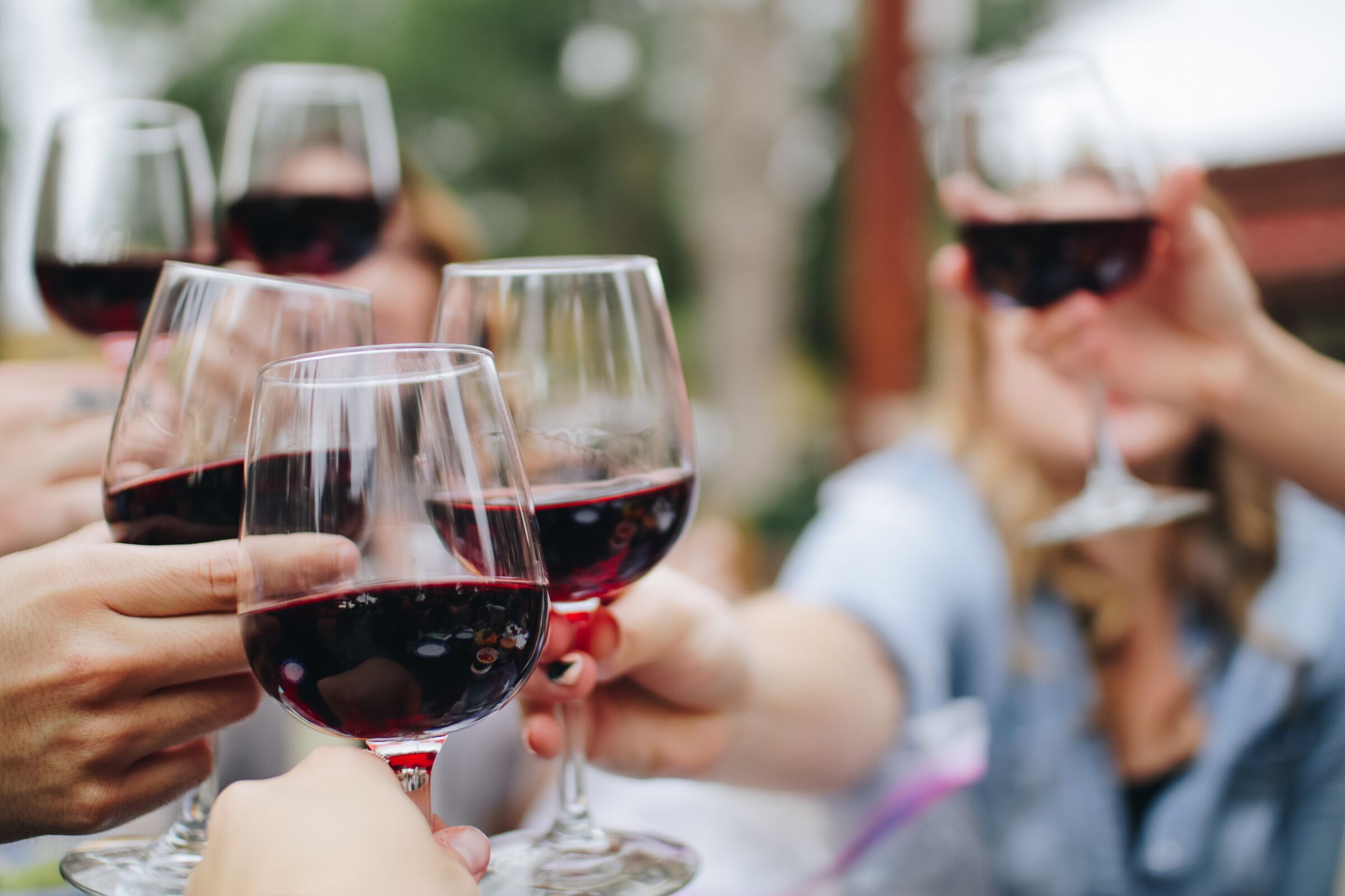 Sechs Hände mit Rotwein in der Hand stoßen an
