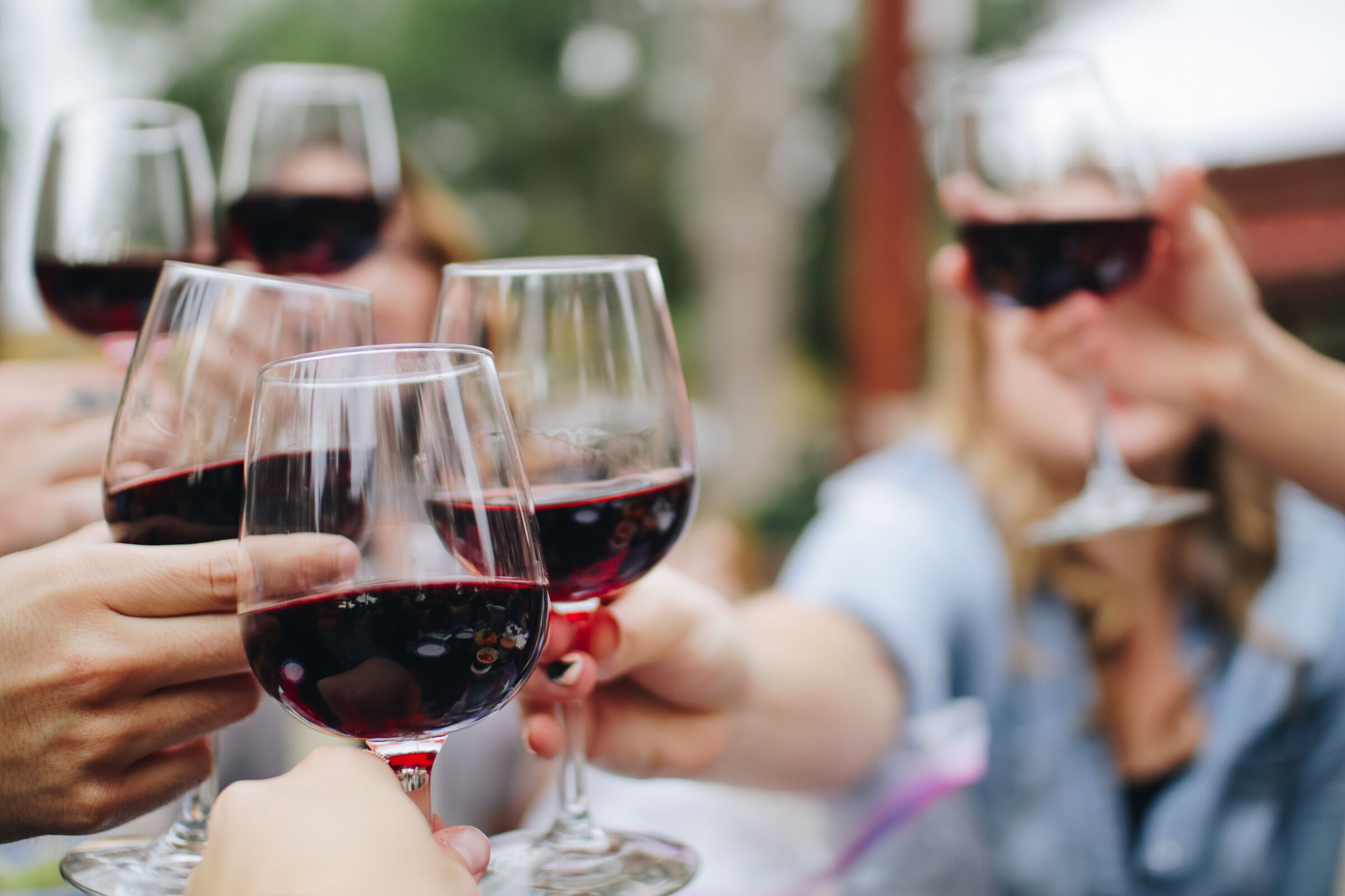 Sechs Hände mit Rotwein in der Hand stoßen an