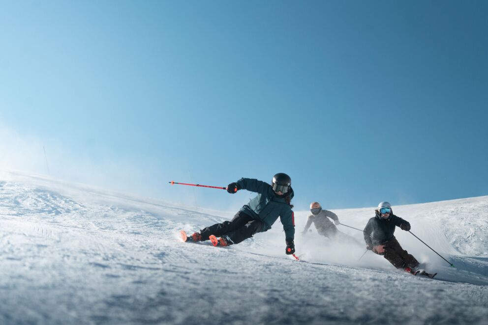 Drei Skifahrer ziehen Schwünge auf einer Piste