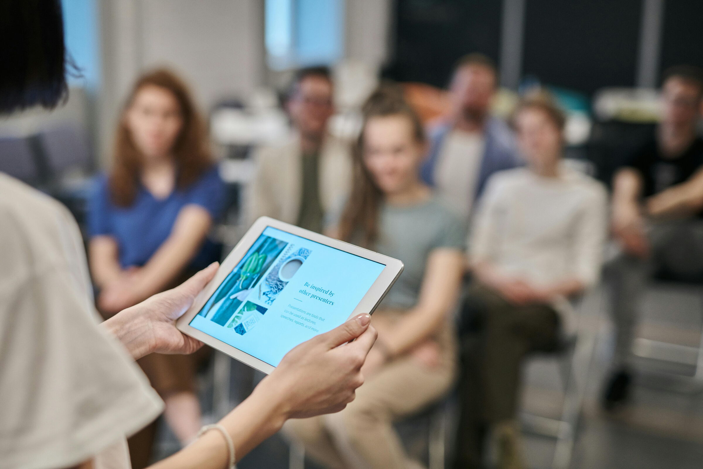 Eine Frau hält ein iPad, im Hintergrund sitzen Menschen