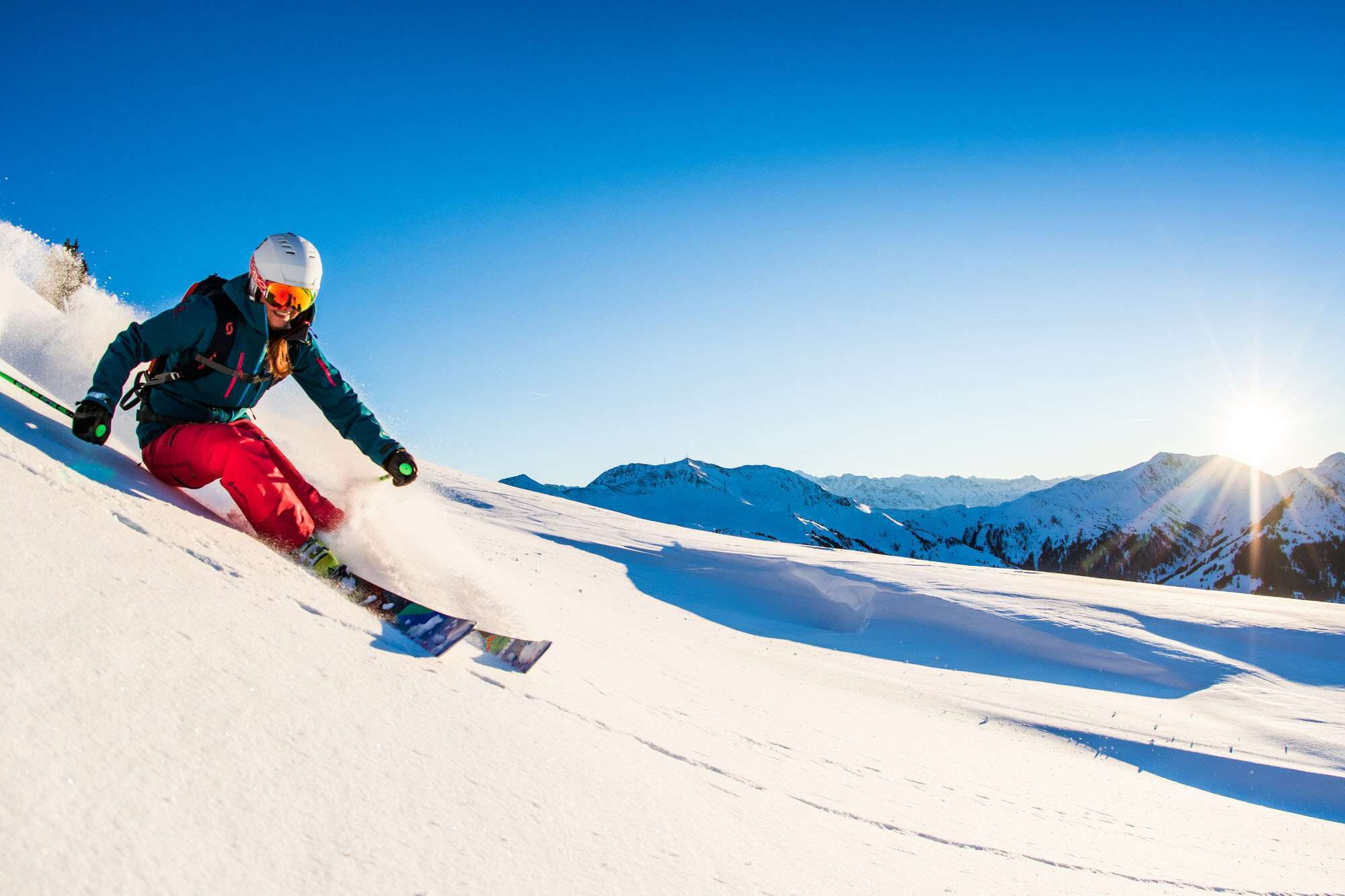 Eine Person im rot-grünen Schneeanzug fährt Ski und wirbelt Schnee auf