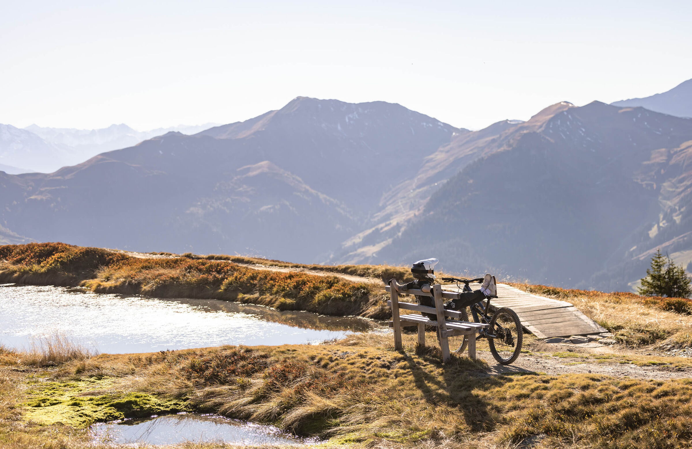 Mountainbiker rastet auf einer Bank neben einen Bergsee in Saalbach Hinterglemm