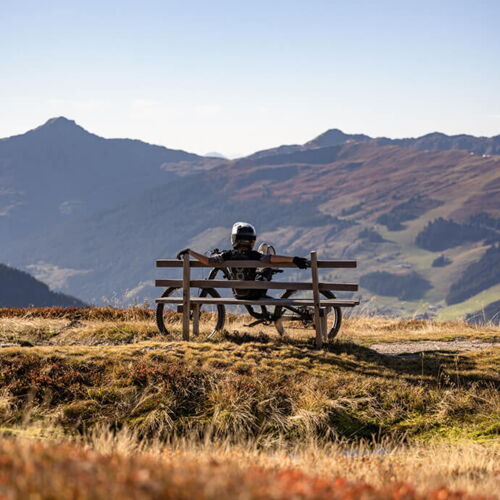 Ein Fahrradfahrer auf einer Bank mit Ausblick auf die Alpen