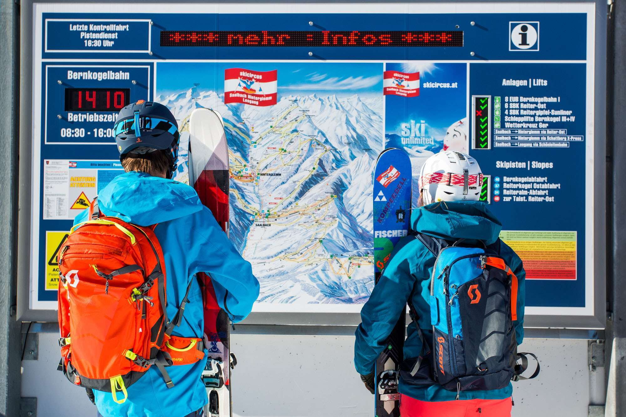 Zwei Skifahrer, die im Ski-In-Ski-Out-Hotel direkt an der Piste urlauben, sehen sich die Infotafel im Skigebiet Saalbach Hinterglemm an.