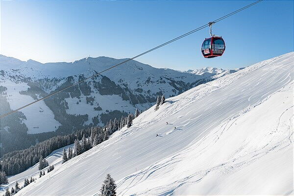 Drei Skifahrer auf einer Piste mit weitem Panorama und eine Liftgondel