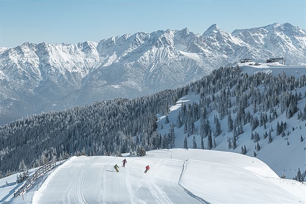 Drei Skifahrer auf einer Piste vor winterlicher alpiner Kulisse